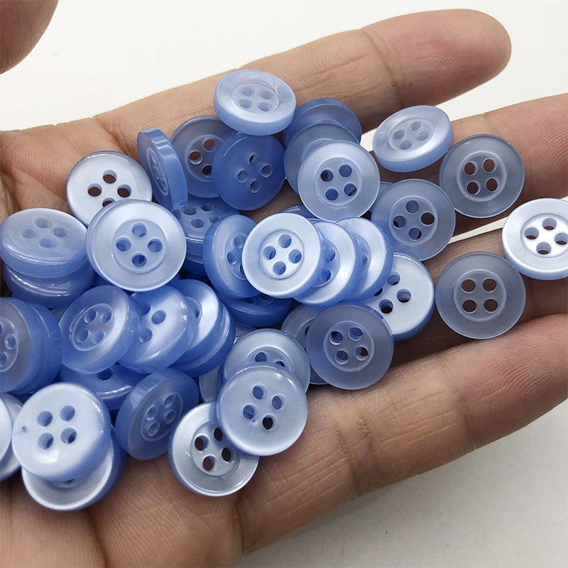 Round 4-hole pearlized resin buttons in light blue, in-hand view (10mm)