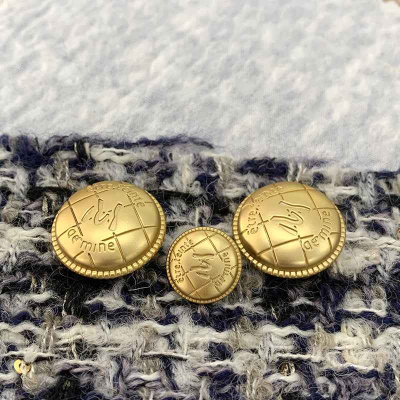 Gold M-letter metal buttons on fabric, round engraved faces with beaded edges