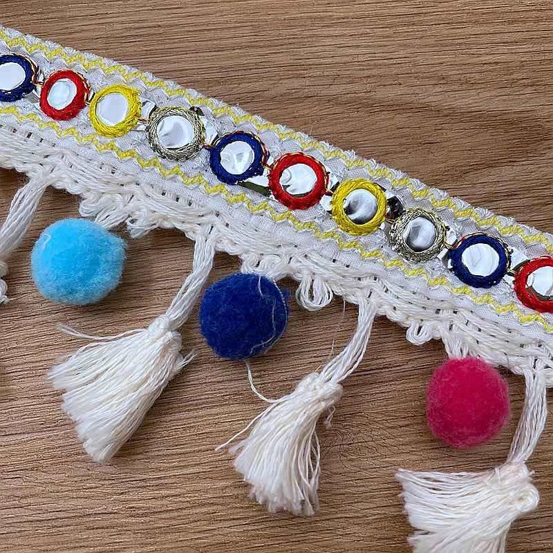 White embroidered trim with multicolor pom-poms and tassel fringe along the edge.