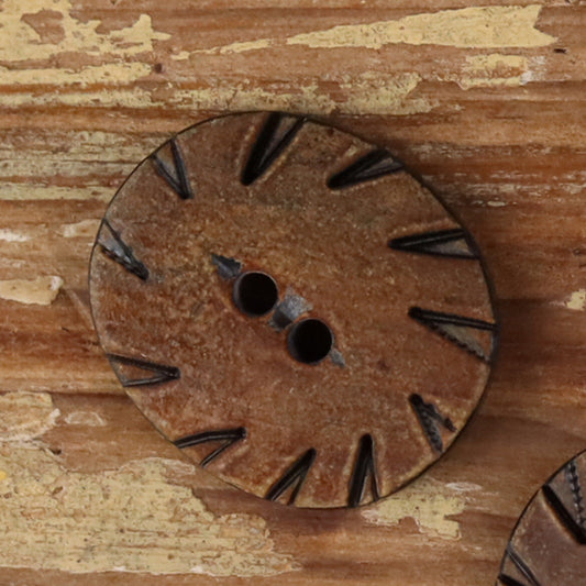 Oval two-hole horn button in brown with carved radial pattern and two-hole center.