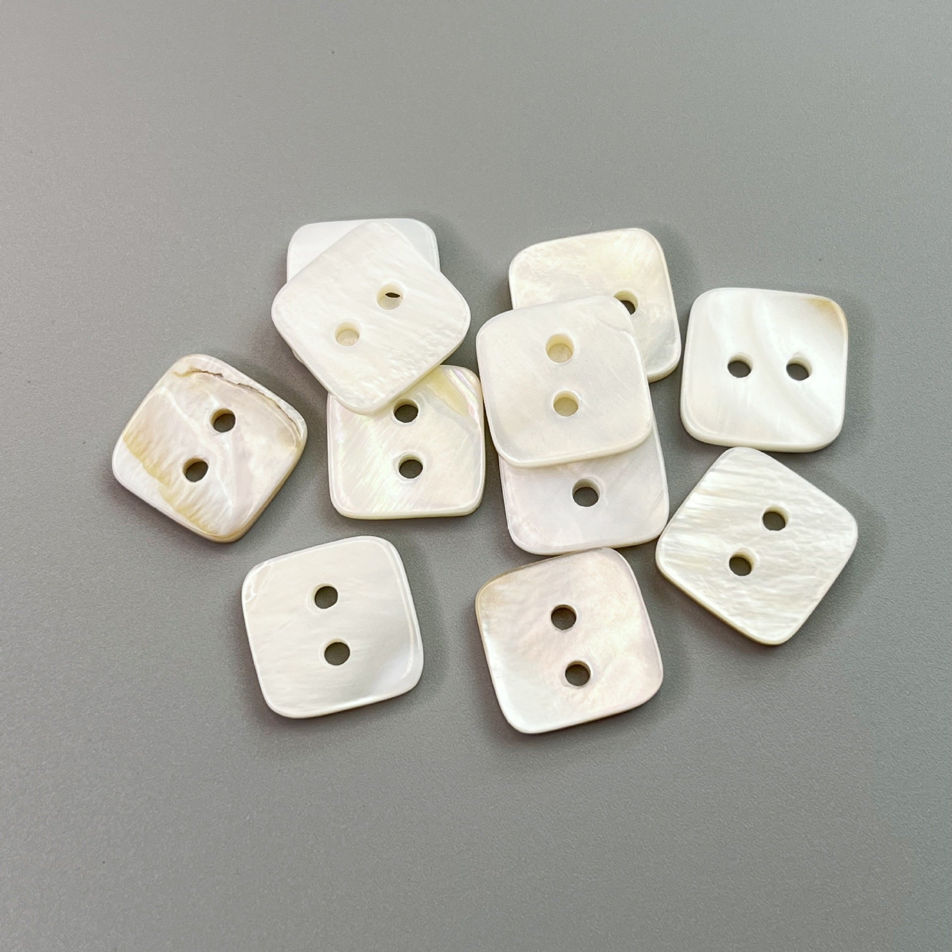 Assorted square two-hole natural shell shirt buttons, off-white with subtle marbling.