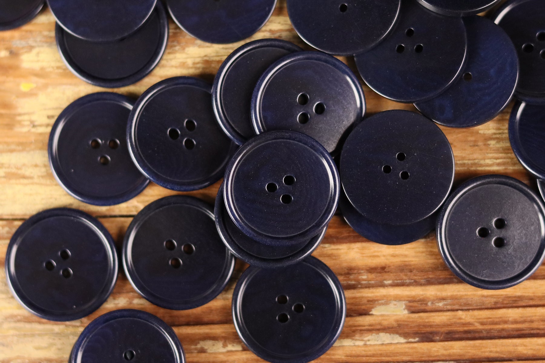 Assorted navy round 3-hole buttons with thin rim on wood
