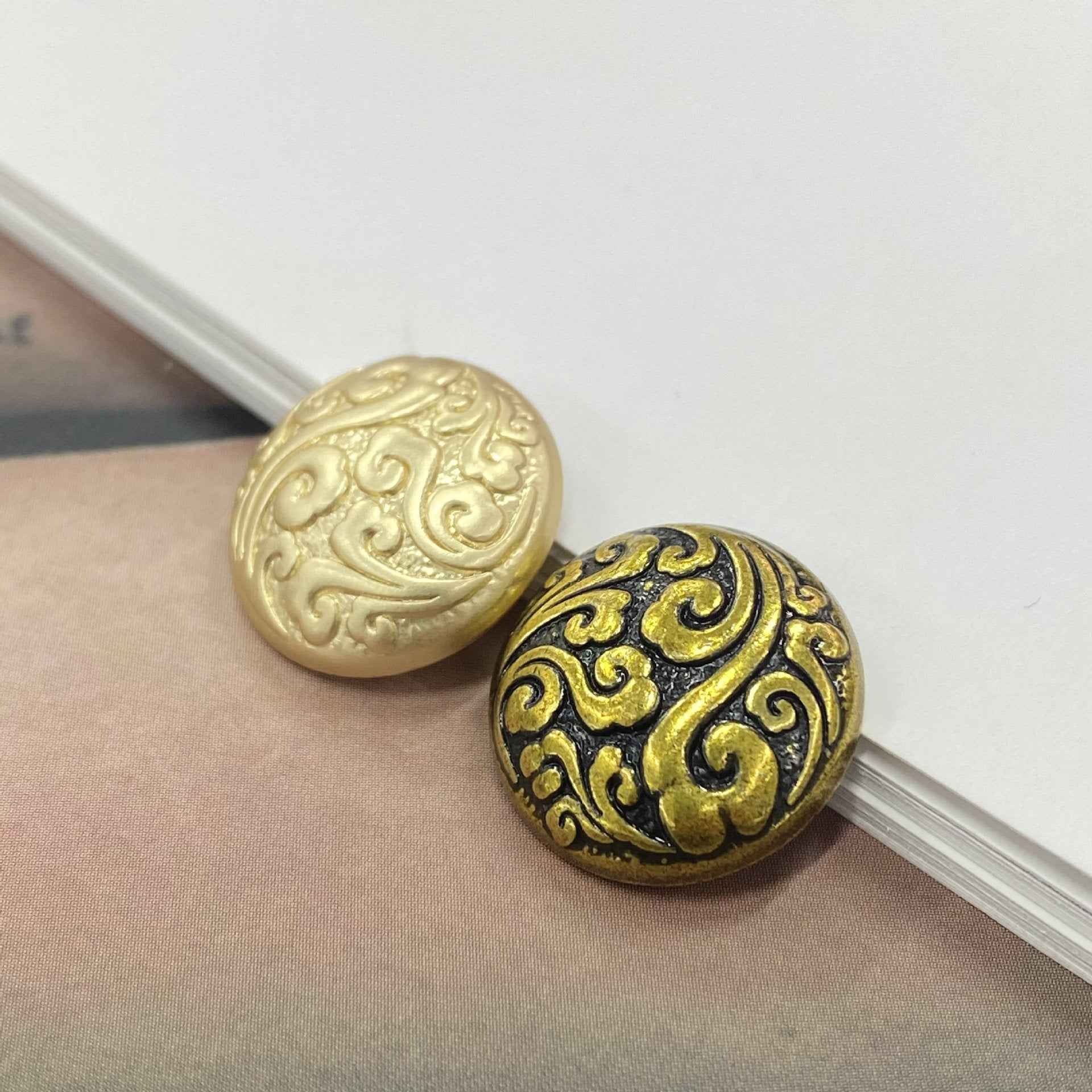 Two cloud-pattern metal shank buttons on ribbon, dark bronze-gold with swirl detailing