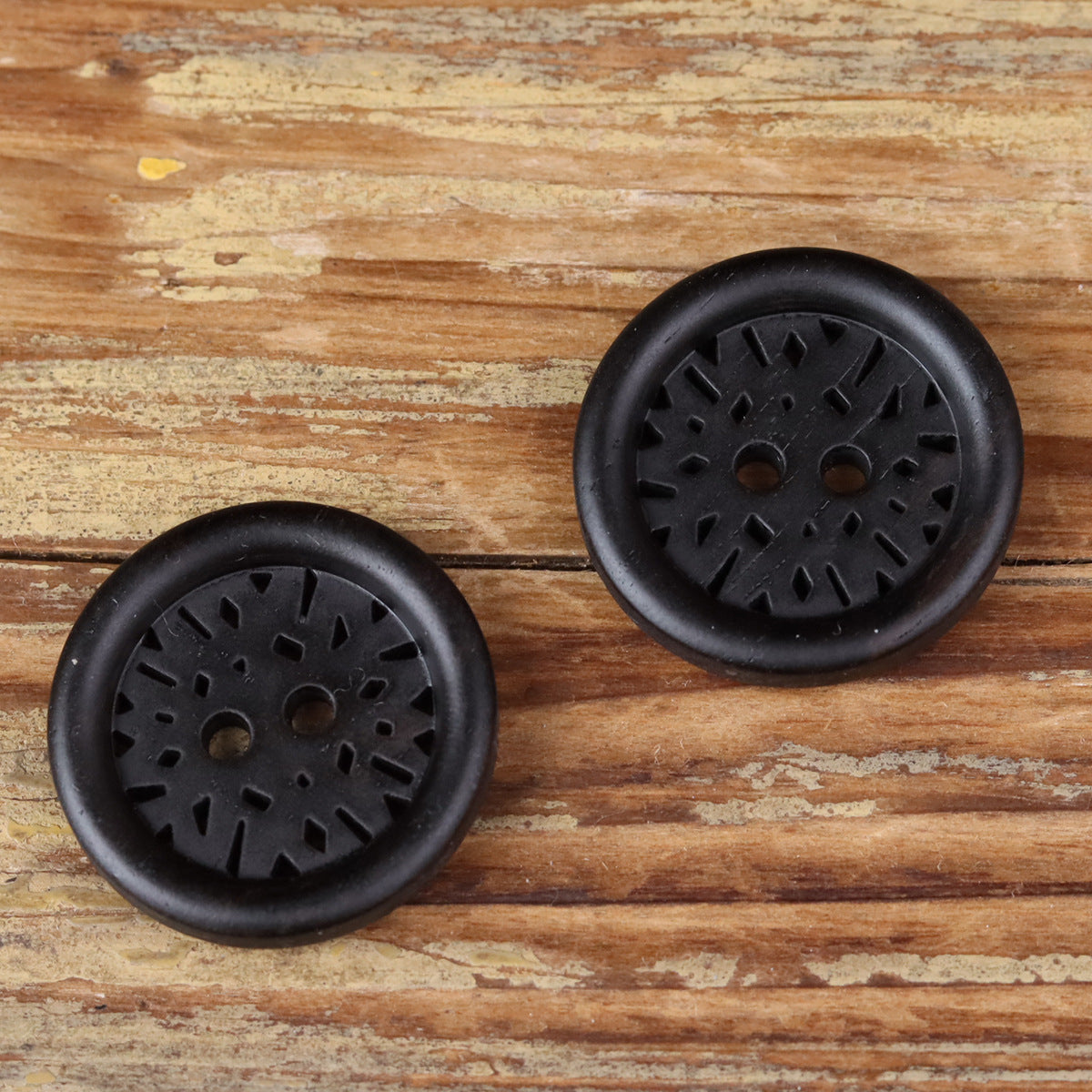 Two round dark 2-hole coat buttons with laser-cut radial pattern, side-by-side