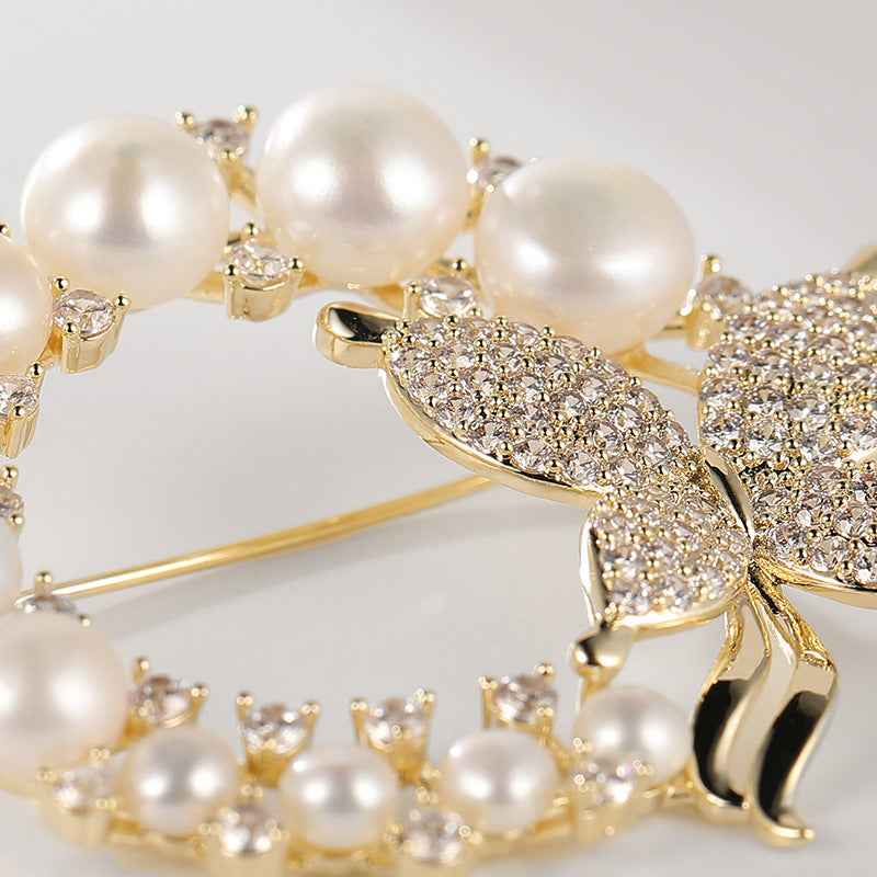 Nahaufnahme: weiße Perlen und funkelnder Strass-Schmetterling auf goldfarbener Brosche