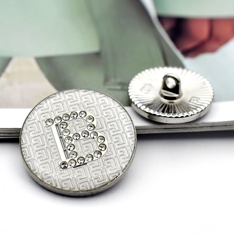 White round button with rhinestone letter 'B' on maze-style geometric background