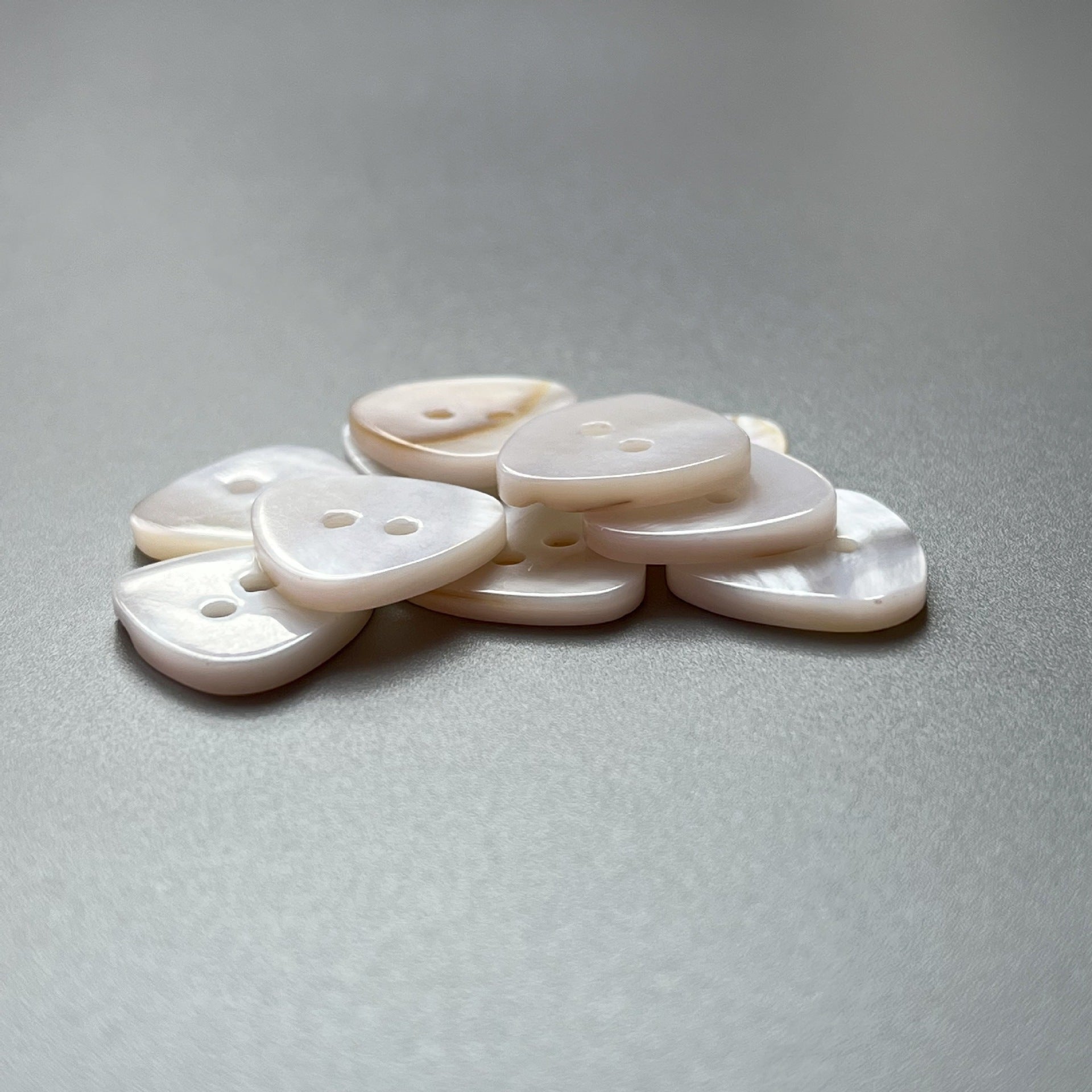 Triangular white shell buttons with two holes, stacked pile of 20