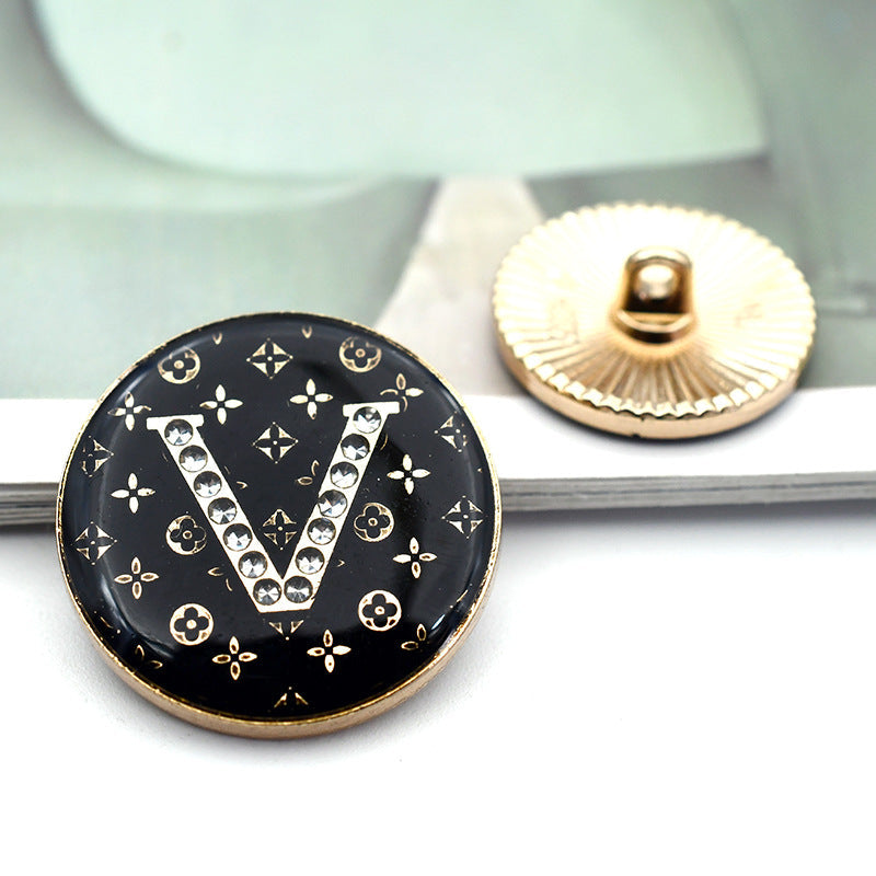 Black round button with rhinestone letter 'V' and small floral icon details