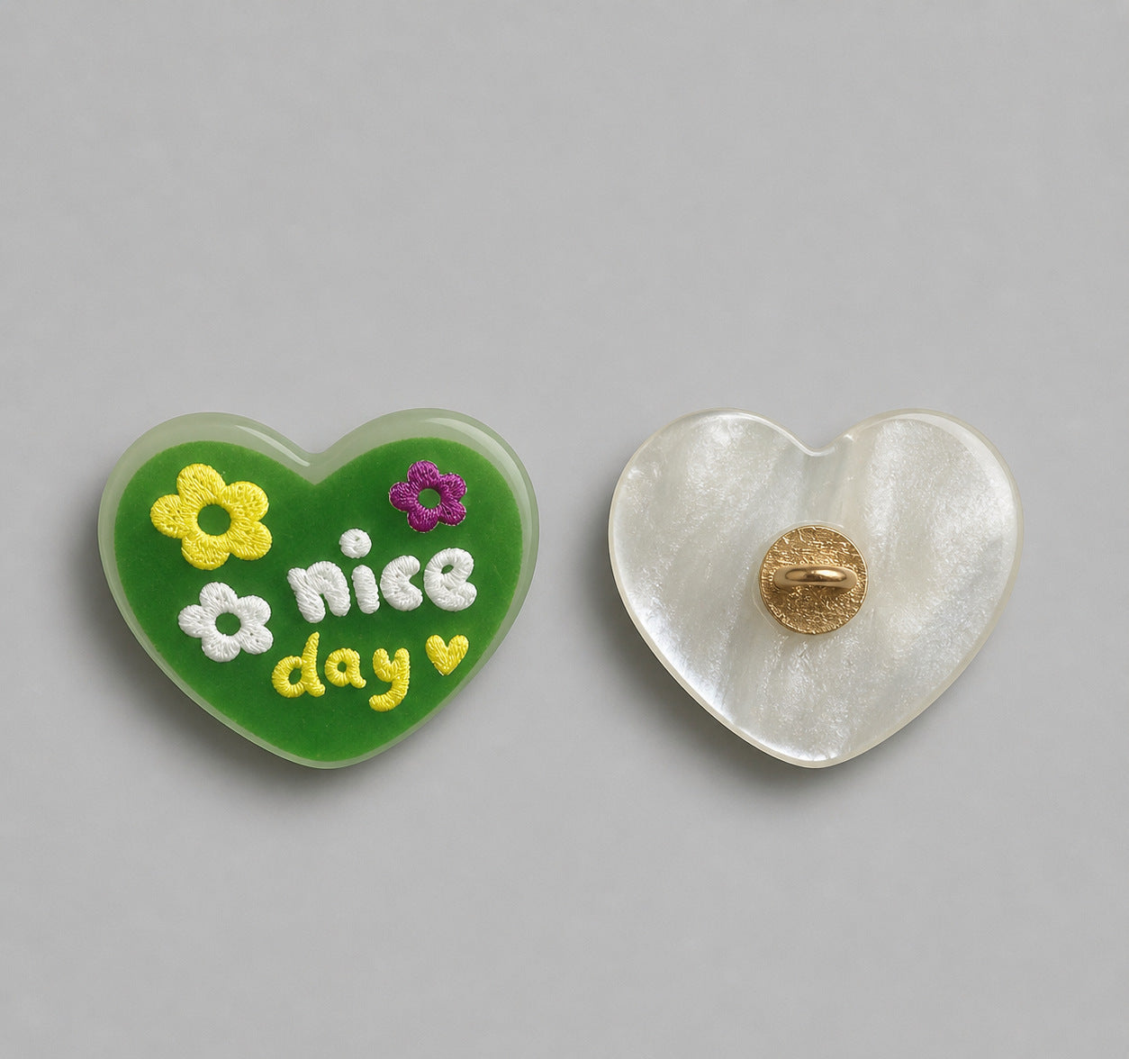 Green heart-shaped resin button with “nice day” and flowers; white back with gold pin