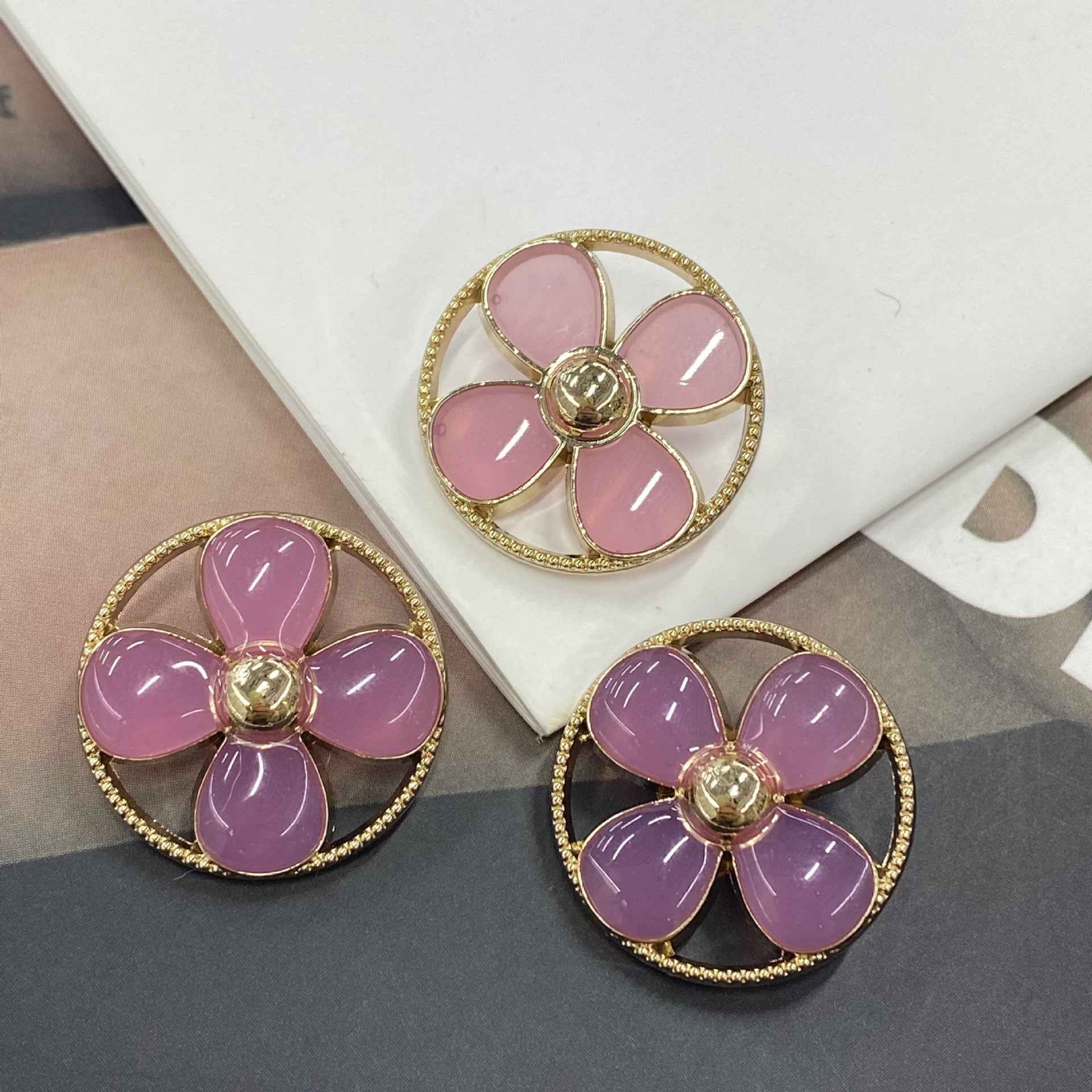 Round clover shank buttons with pink/purple petals, gold-tone rim and central metal shank