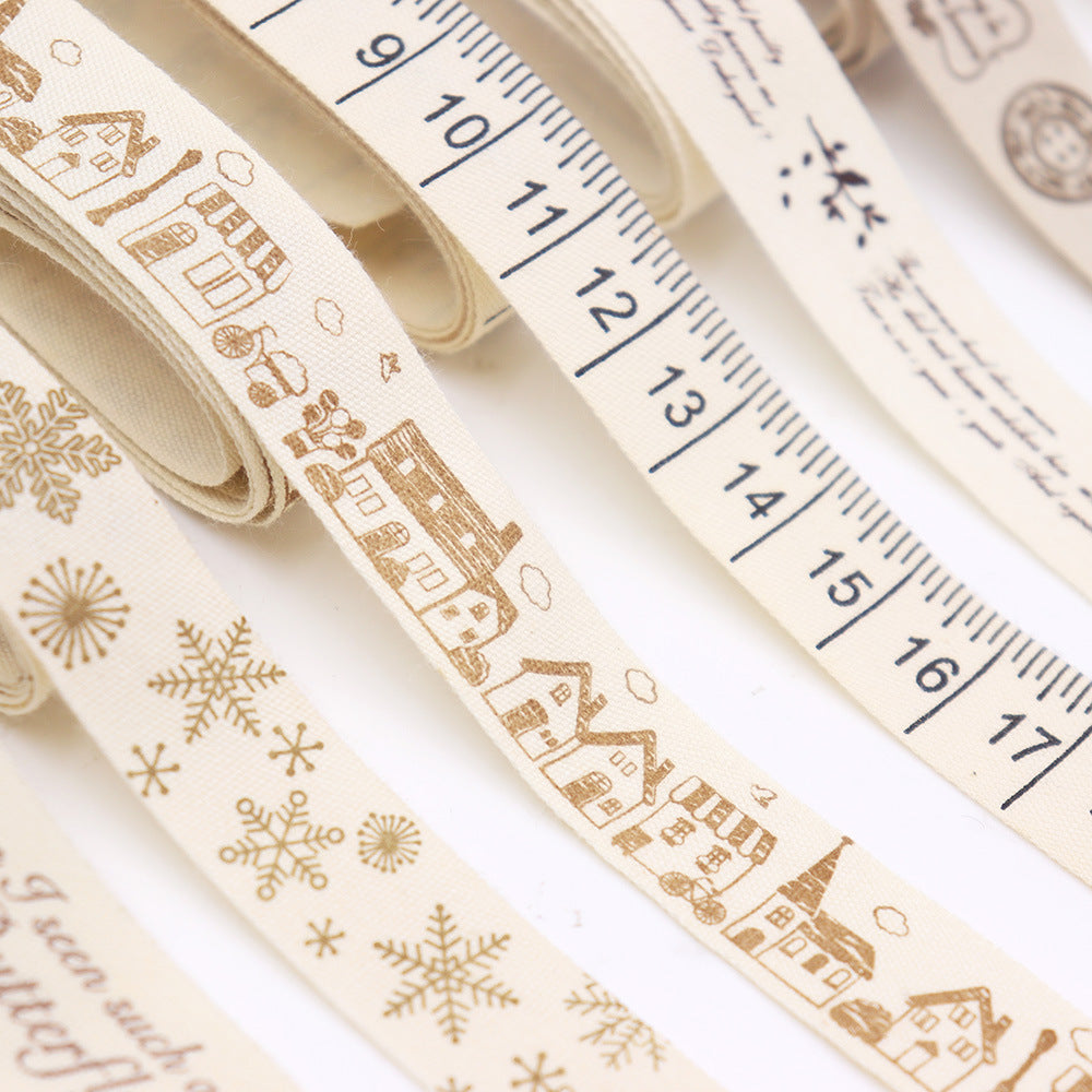 Nahansicht: cremefarbenes Schrägband mit goldenen Winterhäuschen-Illustrationen und Maßband-Optik