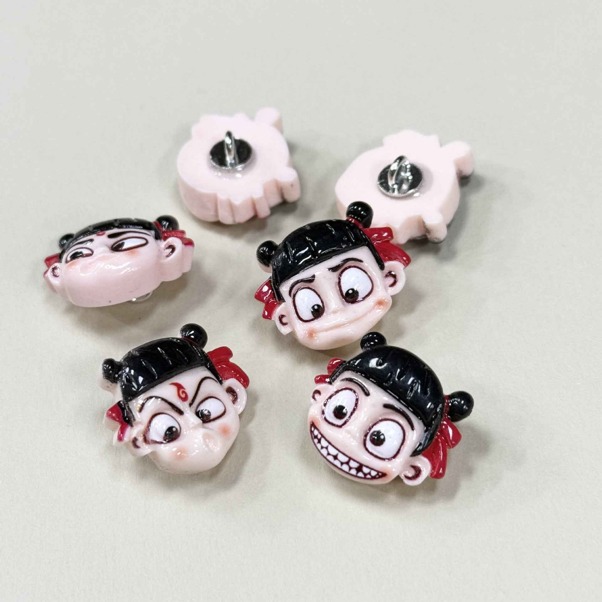 Cartoon Nezha emoji buttons, backs show metal shanks, black hair, red accents