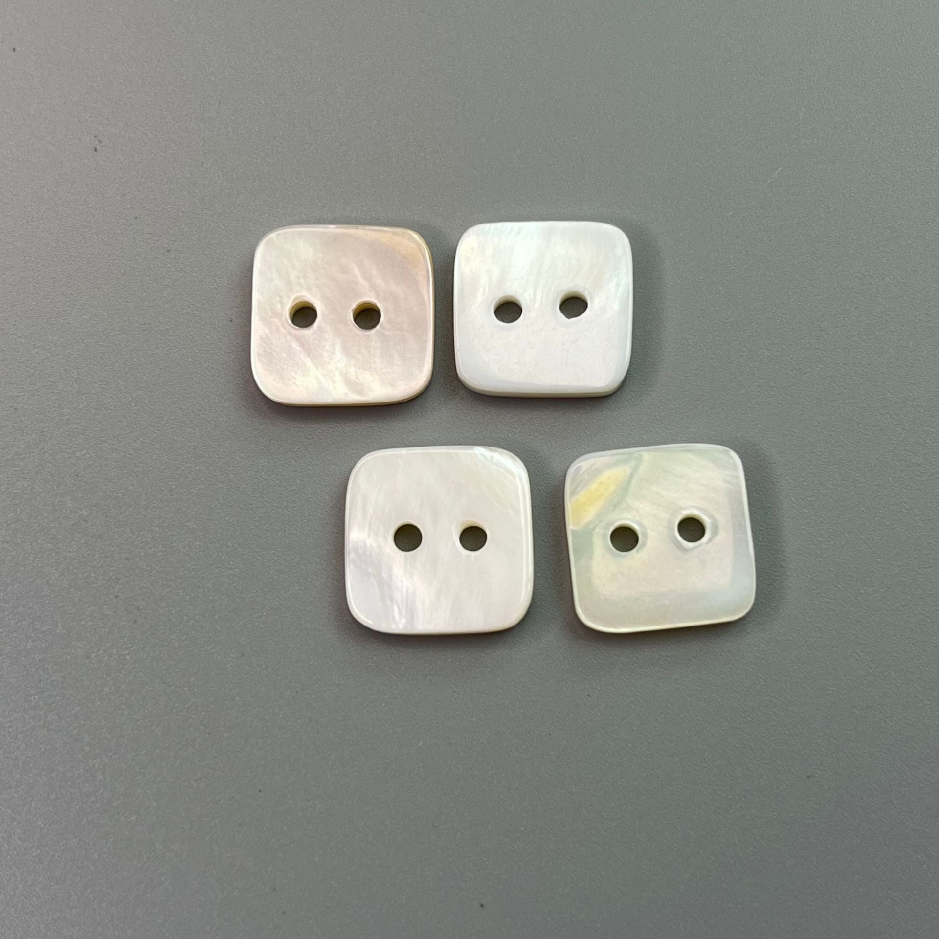 Four square two-hole natural shell shirt buttons, off-white with pearly sheen.