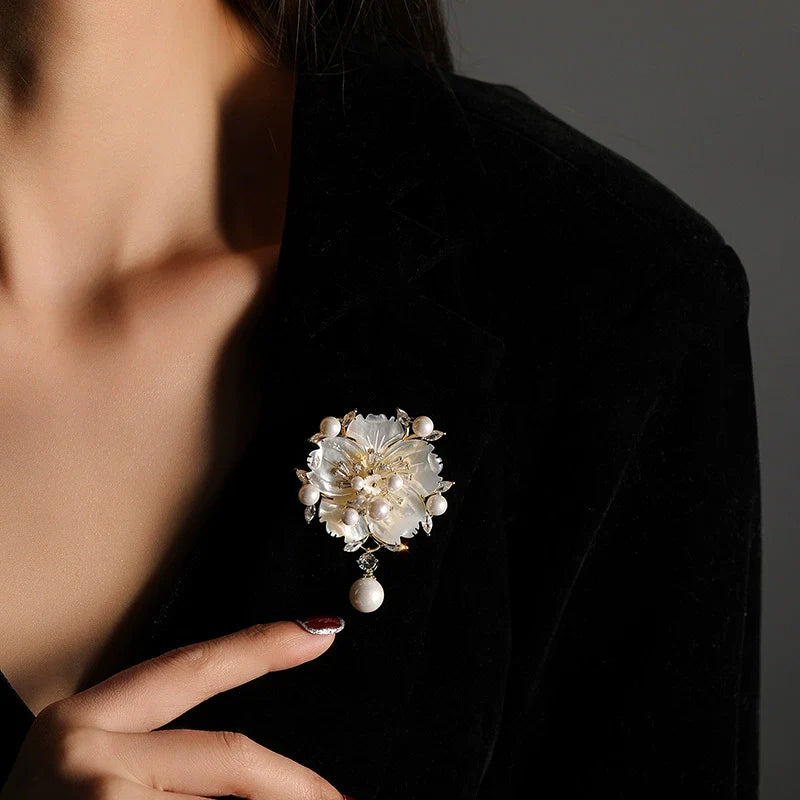 Camellia shell pearl brooch with white petal layers, gold-tone details, hanging pearl