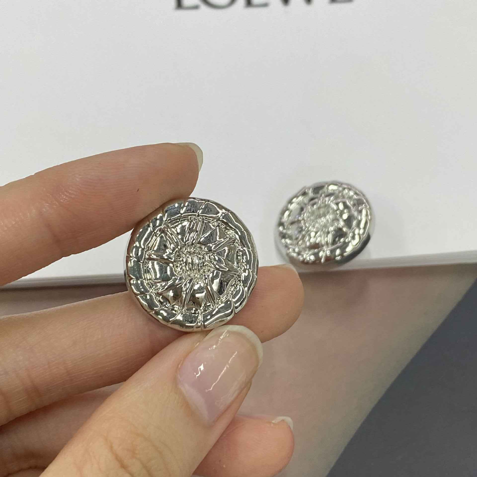 White-silver round 3D metal shank button close-up in hand, embossed floral design