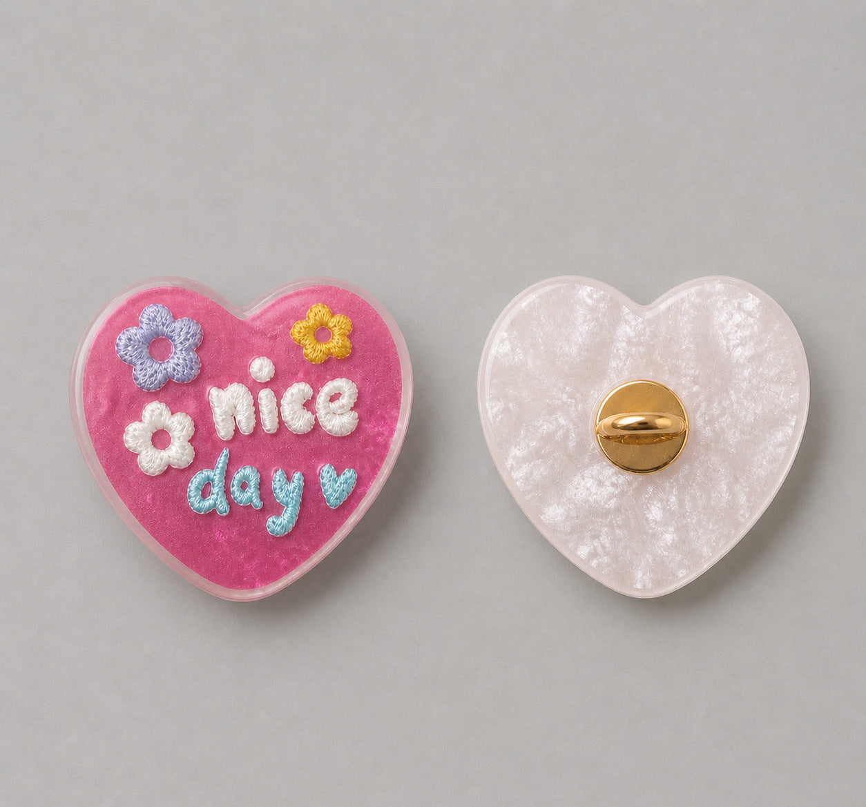 Pink heart-shaped resin button with “nice day” and flowers; white back with gold pin