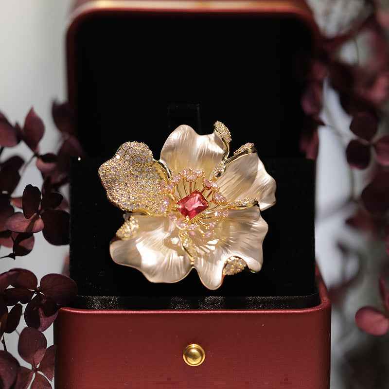 Pfingstrosenbrosche: weiße Blütenblätter, goldfarbene Glitzerumrandung und roter Mittelstein.