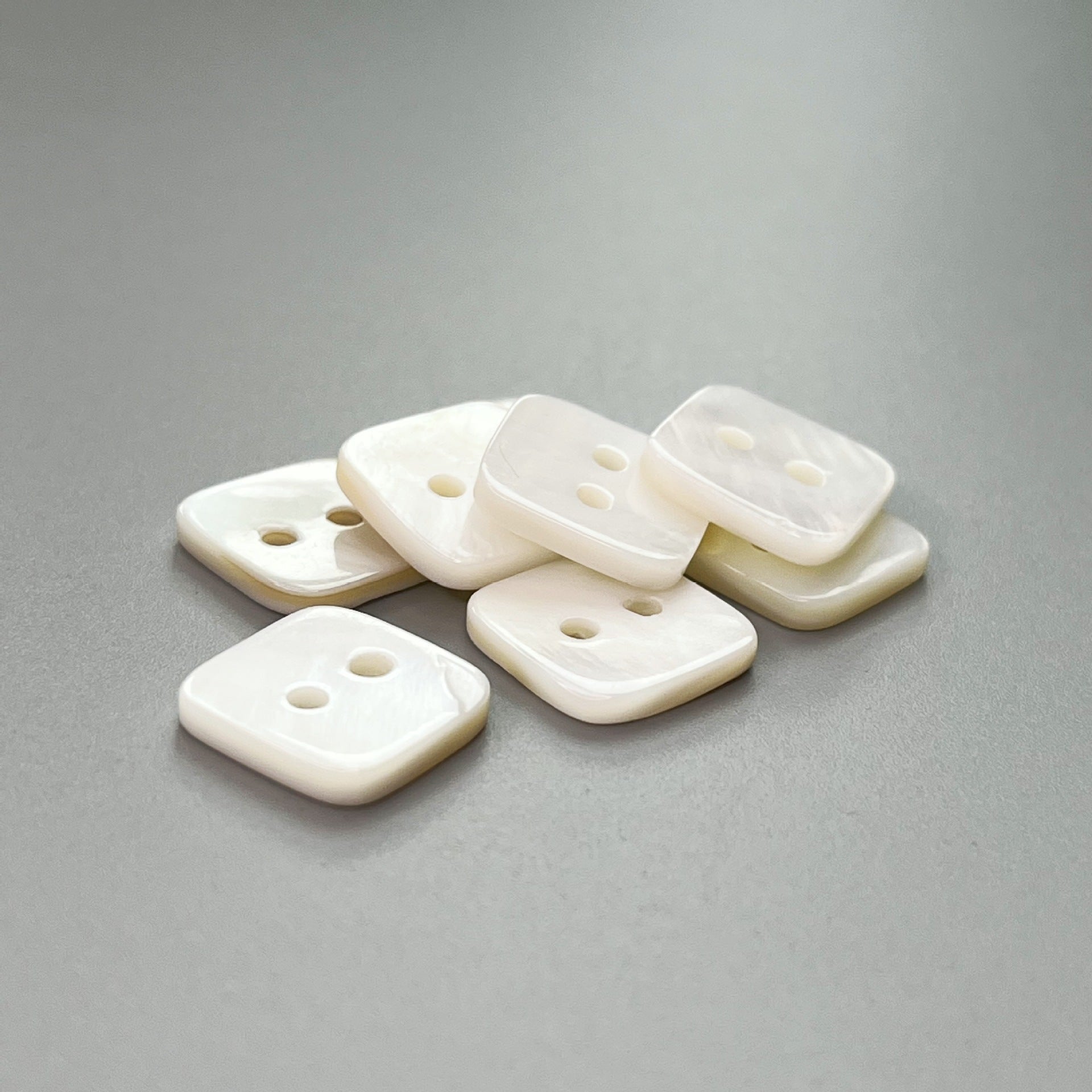 Cluster of square two-hole natural shell shirt buttons in off-white color.