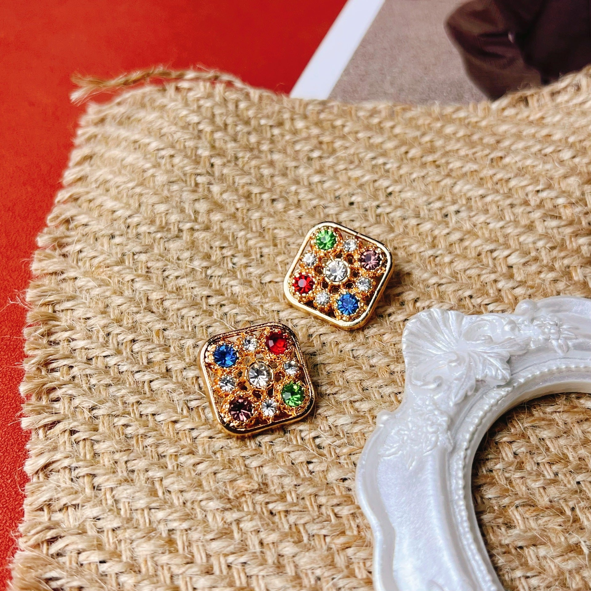 Two square gem sweater buttons on knit fabric, red blue green crystal-like accents