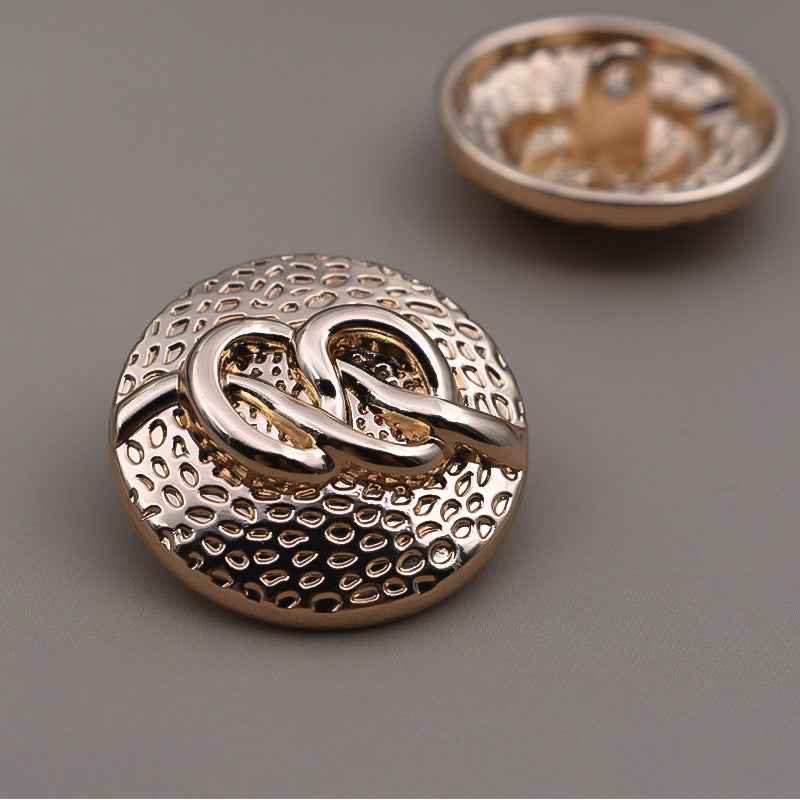 Round antique metal shank button with dotted texture and two-tone swirl design