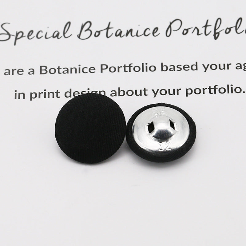 Black fabric-covered shank button with metal shank on underside, round top shown