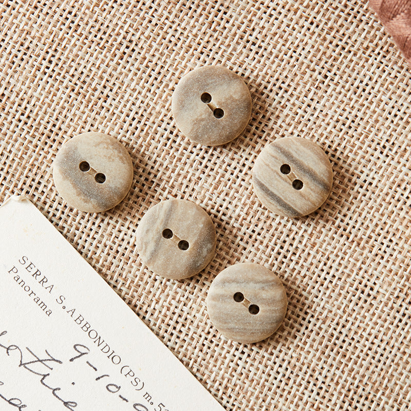 Round two-hole eco-resin buttons, light grey/beige tones on textured fabric