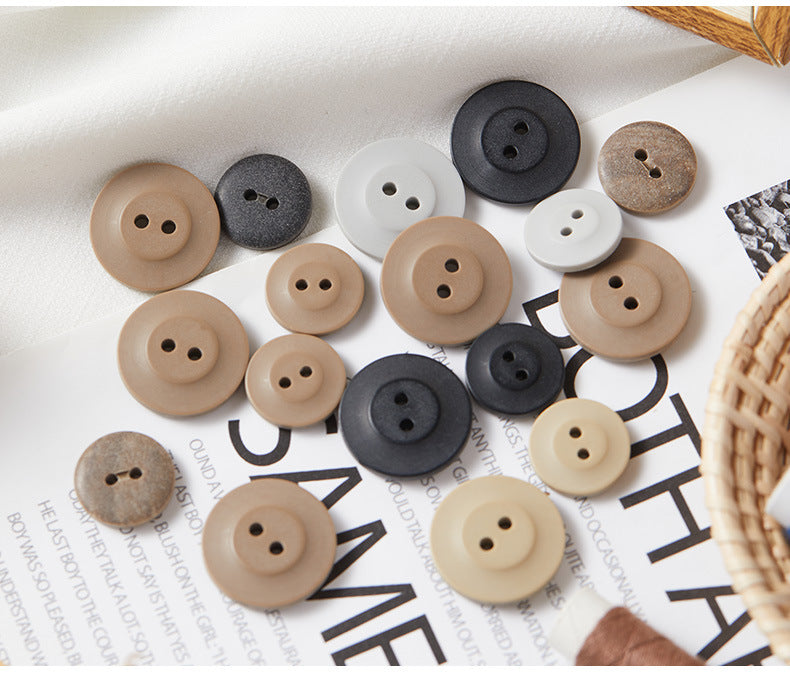 Assorted round two-hole eco-resin buttons in beige, white, and dark tones