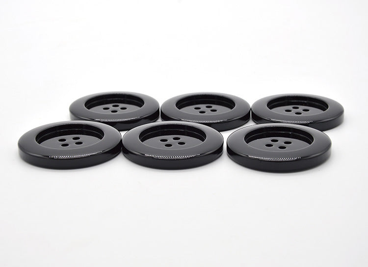 Six glossy black round resin buttons with four holes, front view