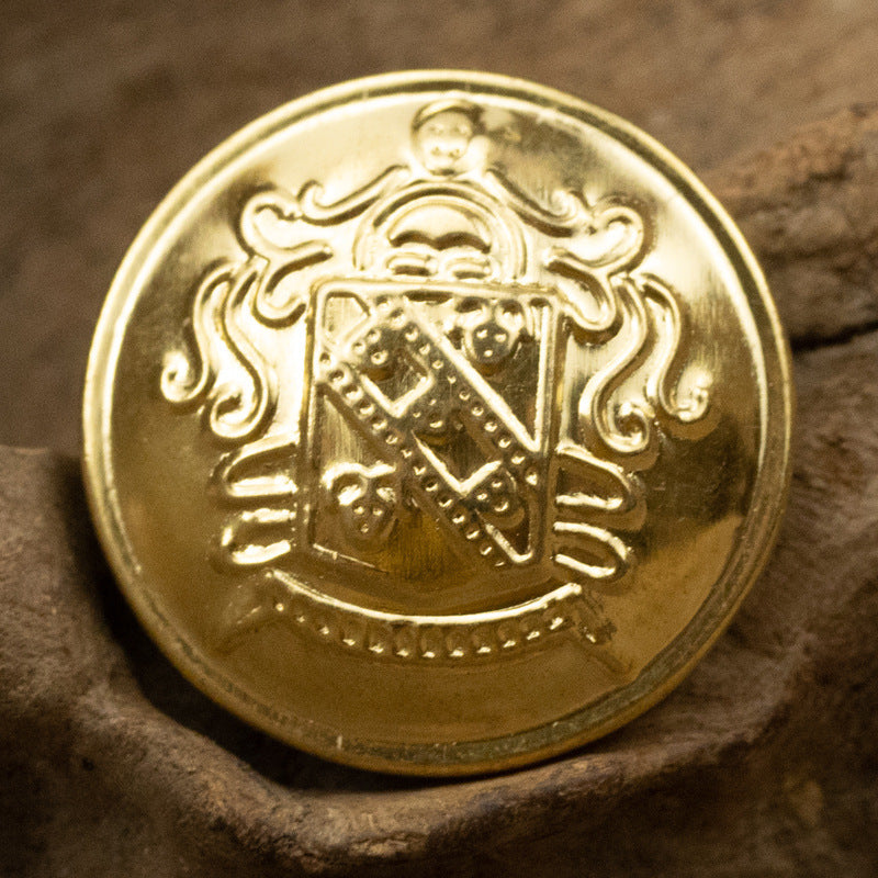 Gold metal shank button close-up front with shield emblem and decorative scrolls