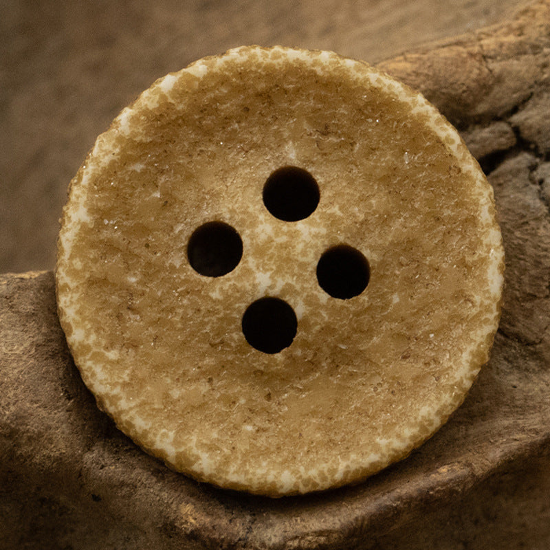 Khaki/beige distressed resin button, four holes, weathered speckled finish.