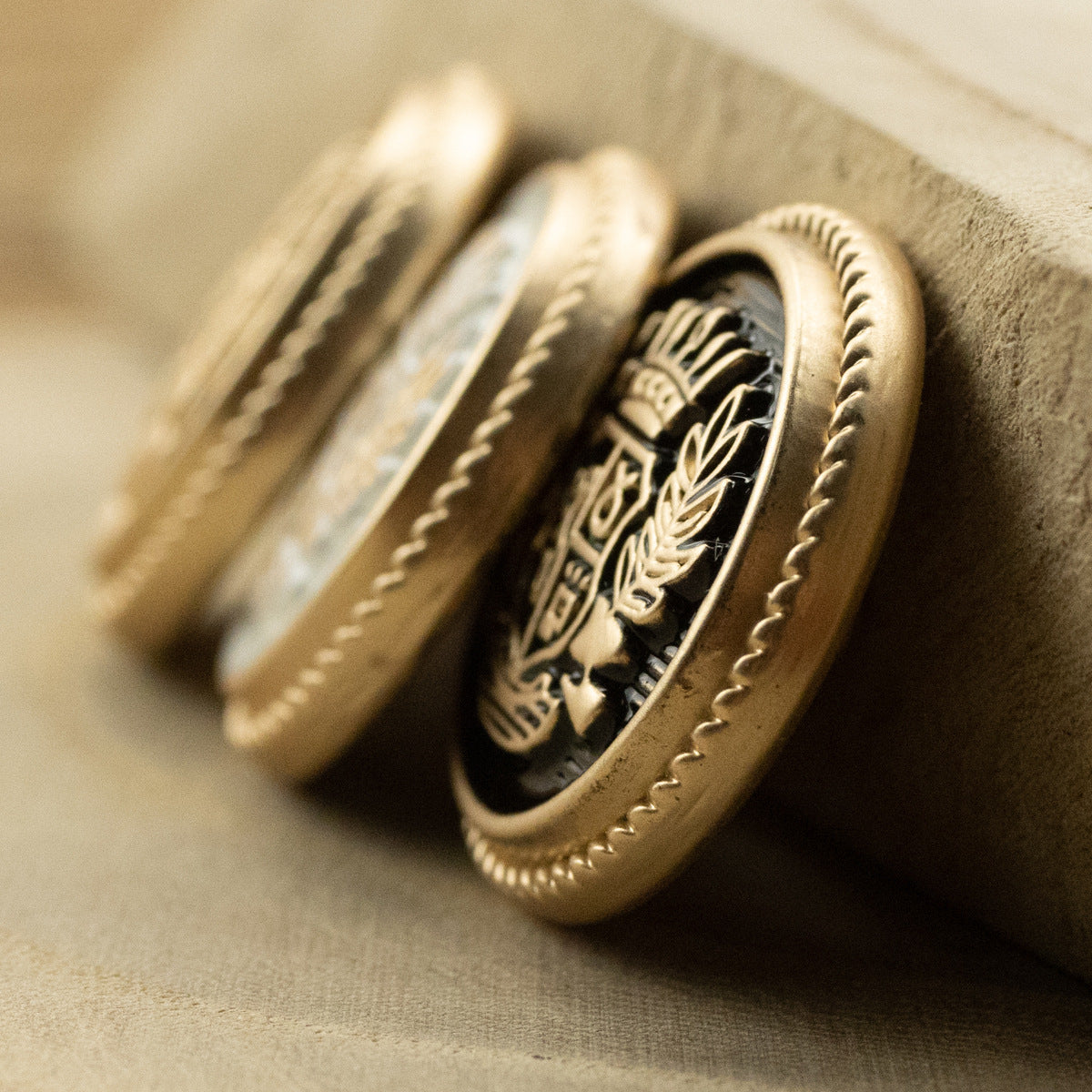 Side view of a gold-tone metal suit button with crown and wheat crest detail