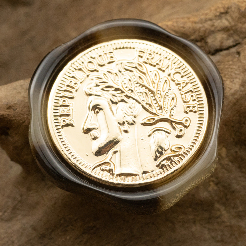 Irregular resin shank button, dark translucent amber, gold portrait medallion