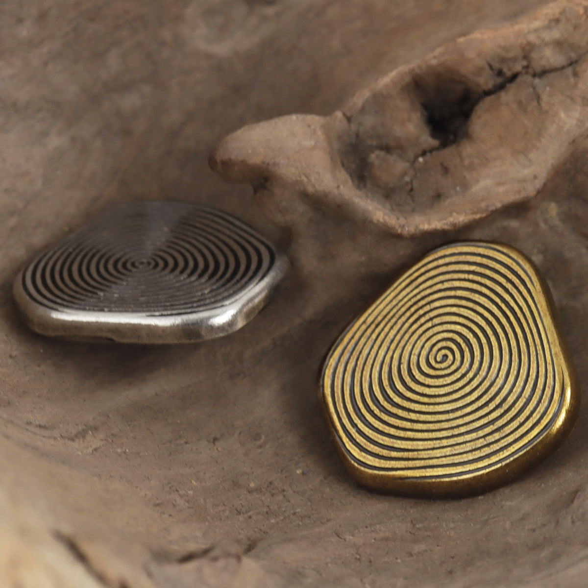 Oval metal shank buttons with concentric swirl lines, one silver, one bronze