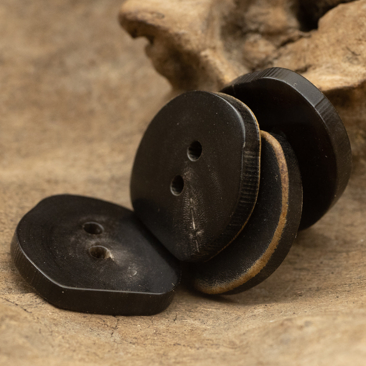 Dark 2-hole horn button pair with irregular shape, front and back views