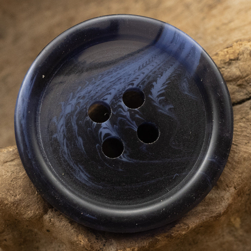 Navy blue round resin button with four holes and subtle mottled pattern