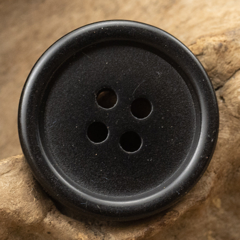 Black round resin button with four holes and fine speckled texture