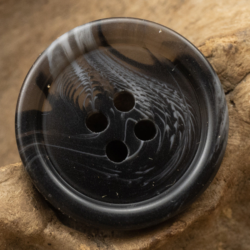 Black round resin button with four holes and smoky gray veining