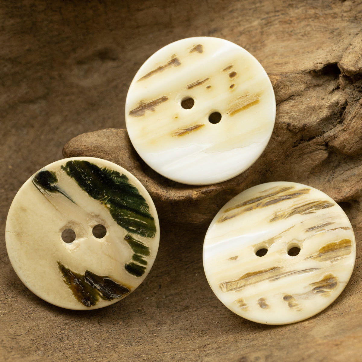 Three classic flat two-hole natural shell buttons with distinct veining patterns