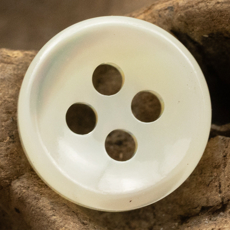 Beige 4-hole shell button with dark back holes, side view