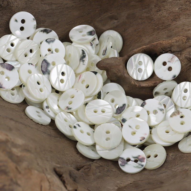 Assorted pile of natural off-white two-hole shell buttons with laser engraving