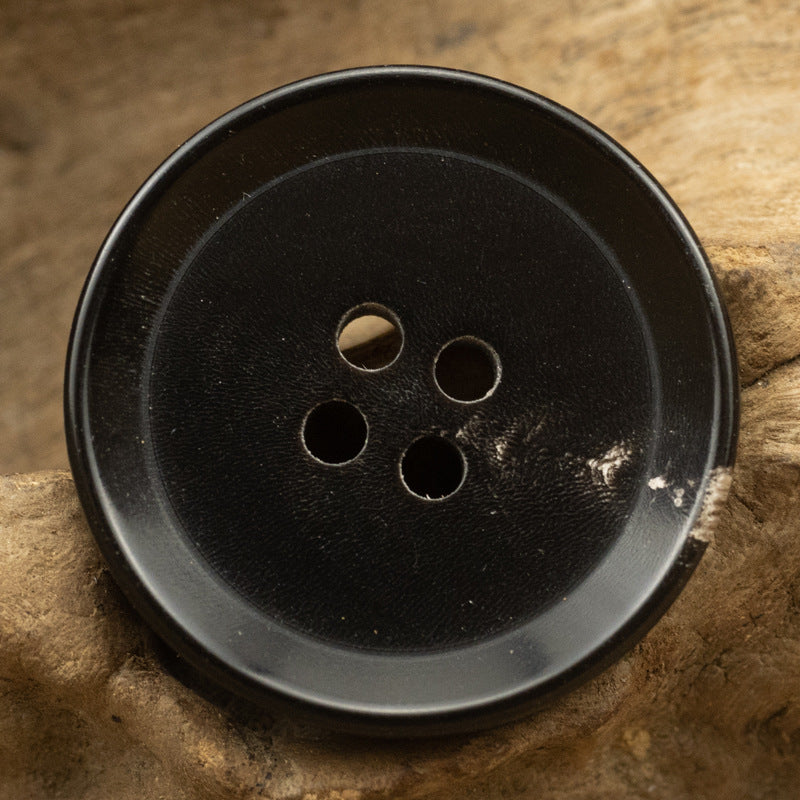Black round button face with four holes, horn-style edge detail