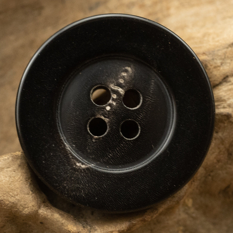 Round black button face with four holes, horn-style texture