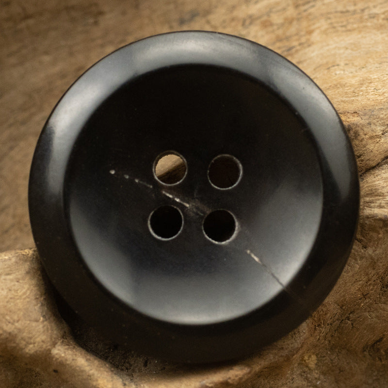 Black horn-style button with four holes, slightly glossy finish