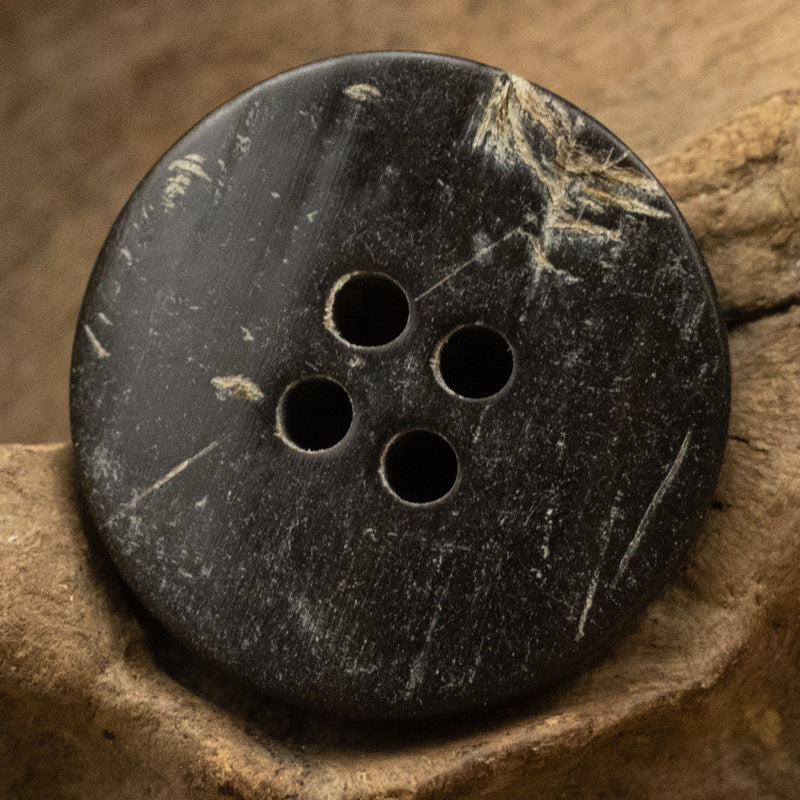 Black horn button, rough uneven texture, round face with 4 holes