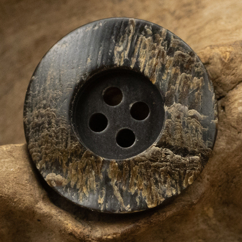 Black horn button close-up, rough grain, round face with 4 holes and dark finish