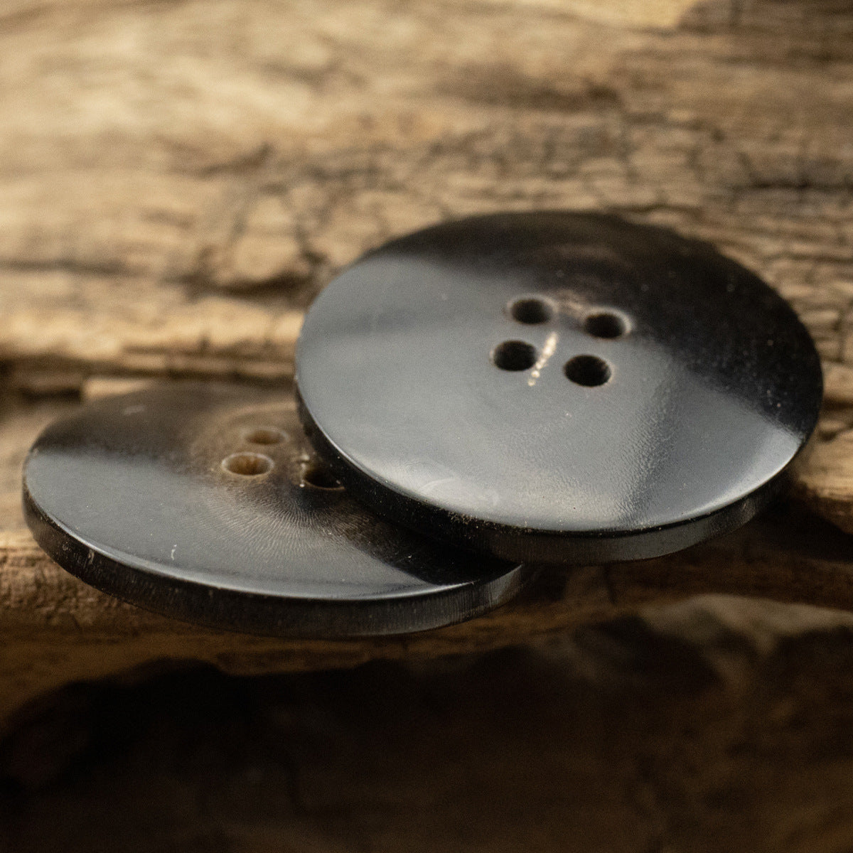 Black horn buttons, 4-hole faces, profile view with smooth edge