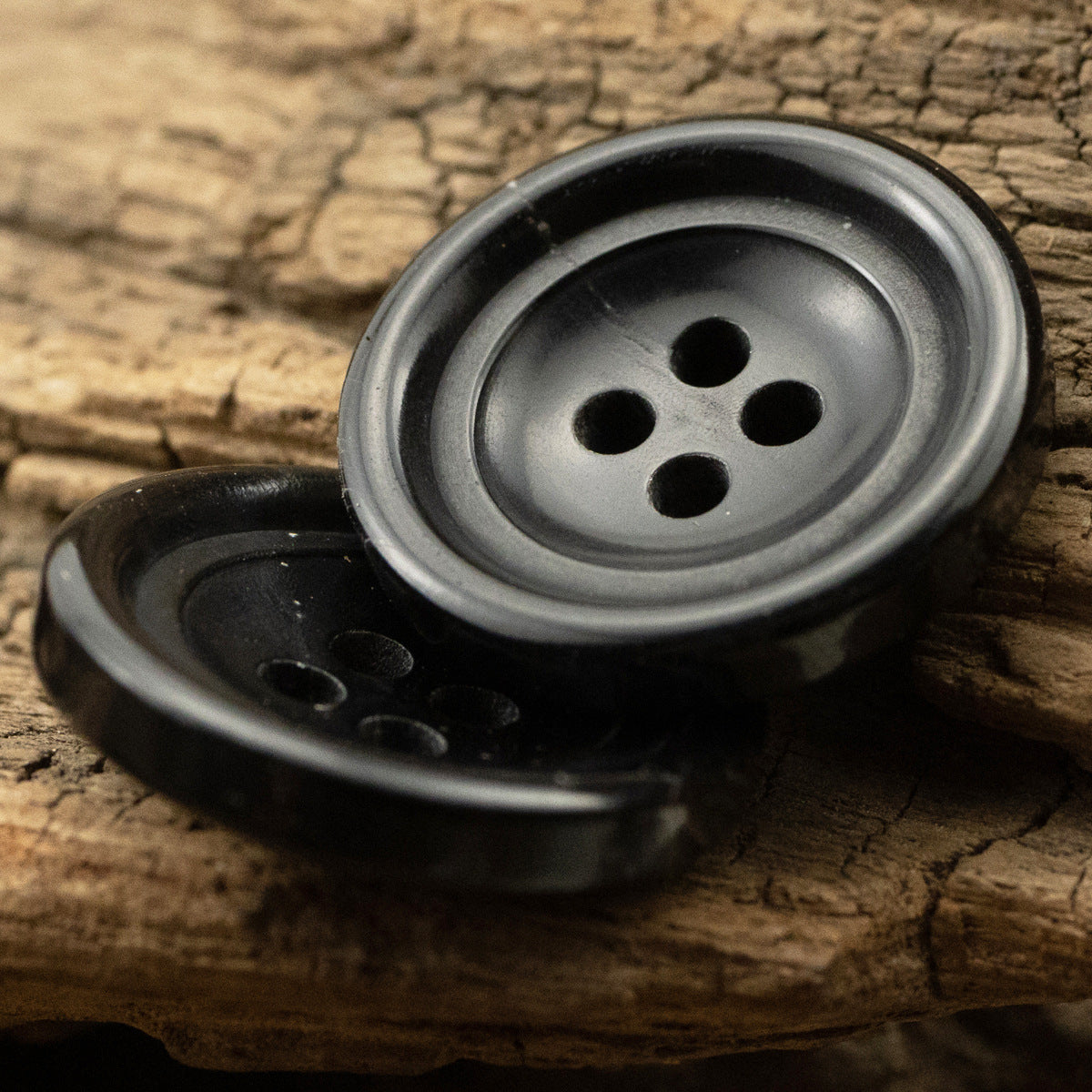 Close-up of black four-hole horn buttons, one face-up, one partially visible