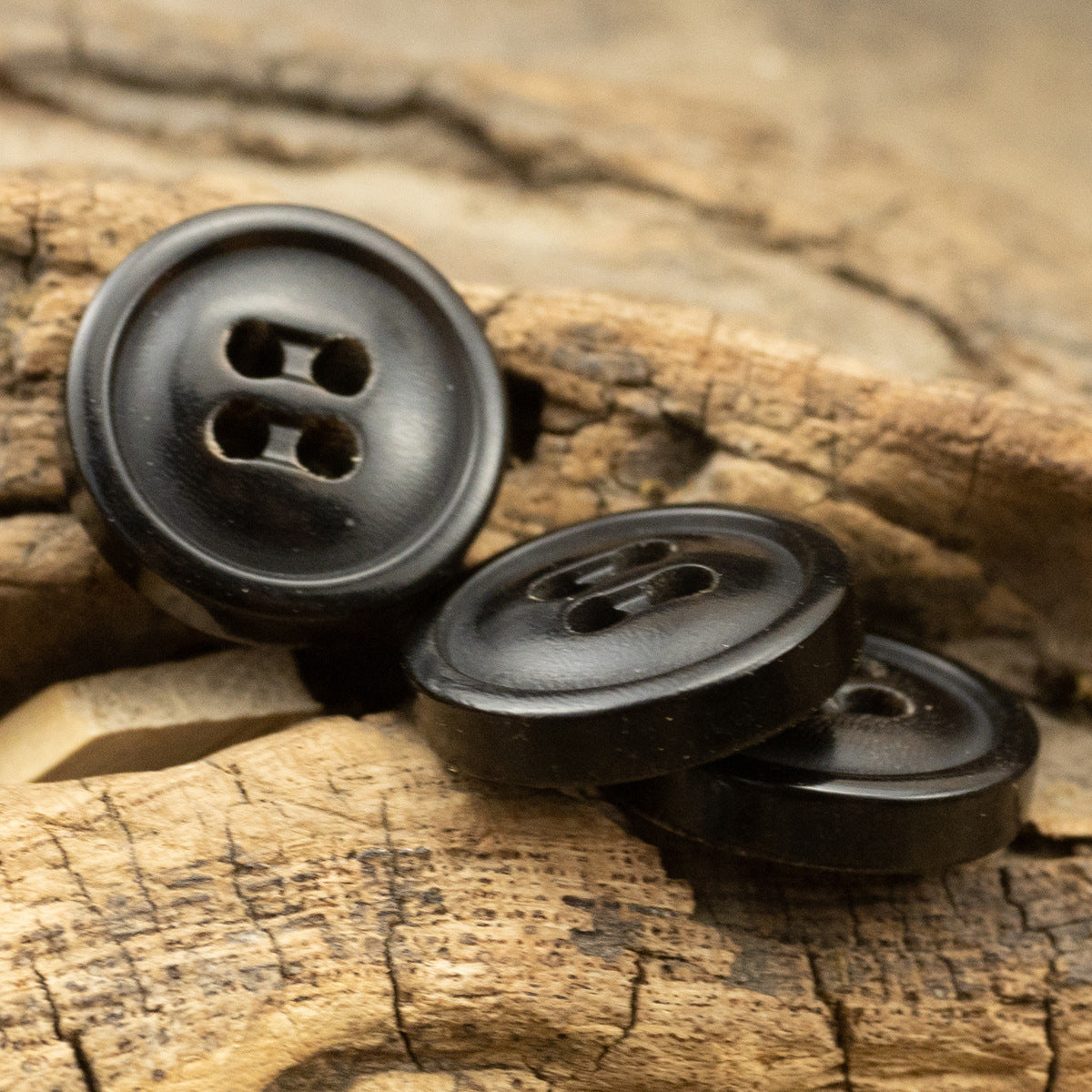 Three natural black horn buttons with round faces and four stitch holes