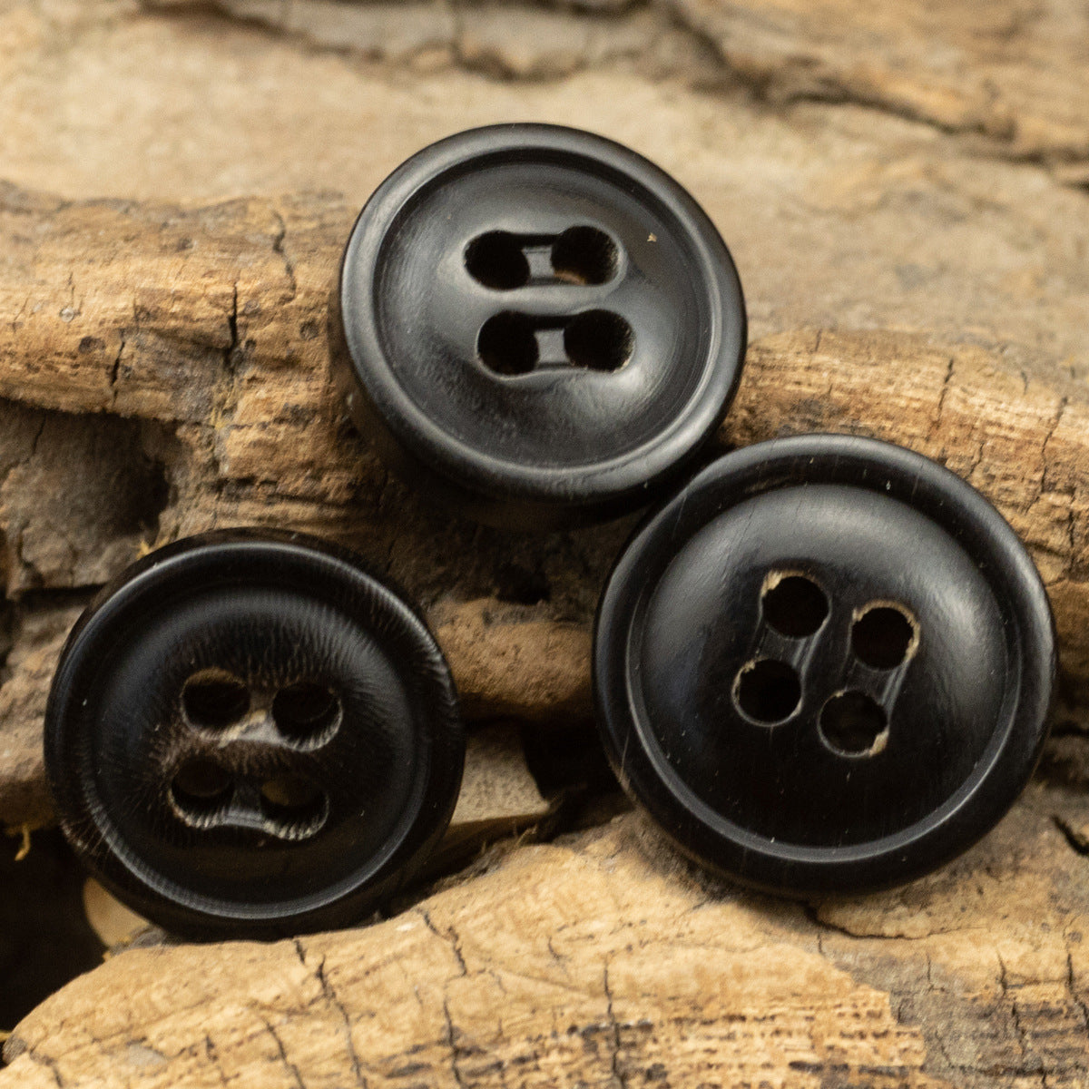Set of three natural black horn buttons with four stitch holes each