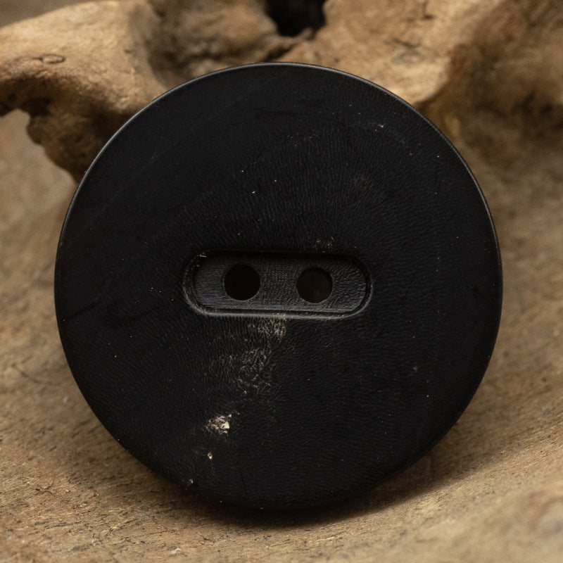 Matte black flat two-hole horn button, close-up, 15–28mm